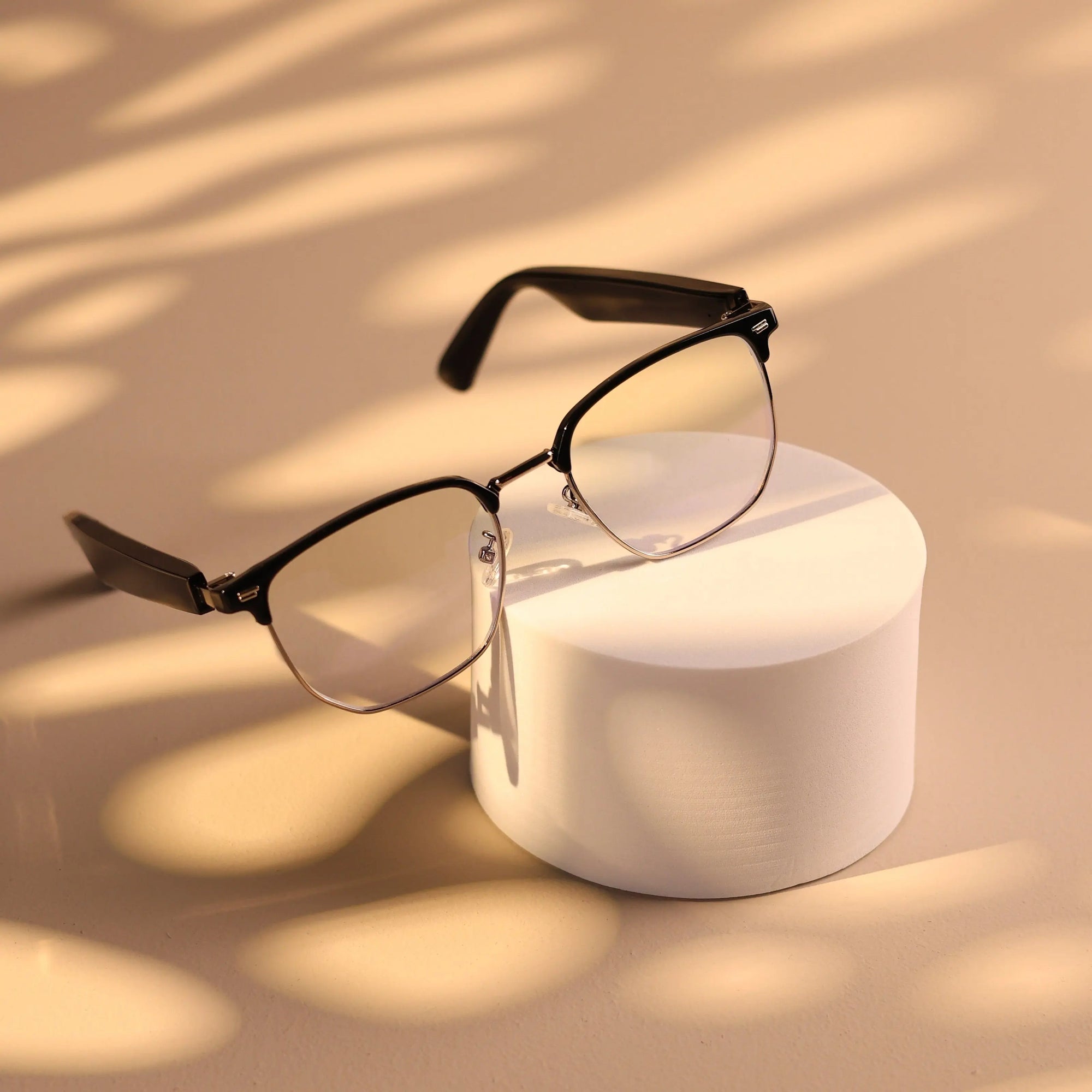 DUSK Halo smart blue light glasses with black frames resting on a white pedestal under warm lighting