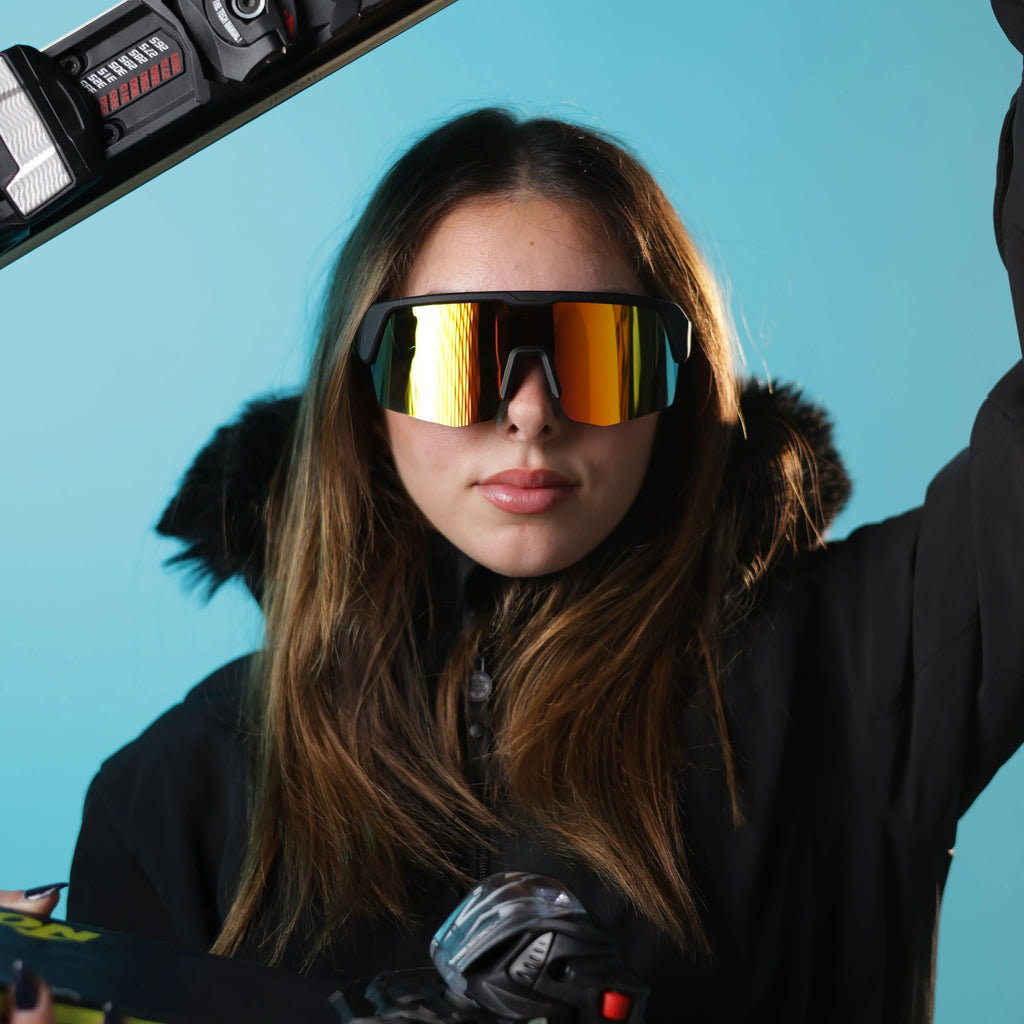 Person wearing reflective goggles holding skis against a blue background