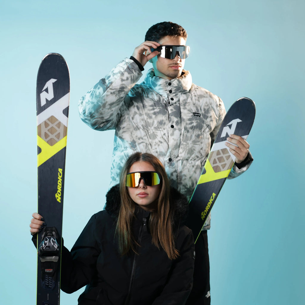 Two people holding skis against a light blue background
